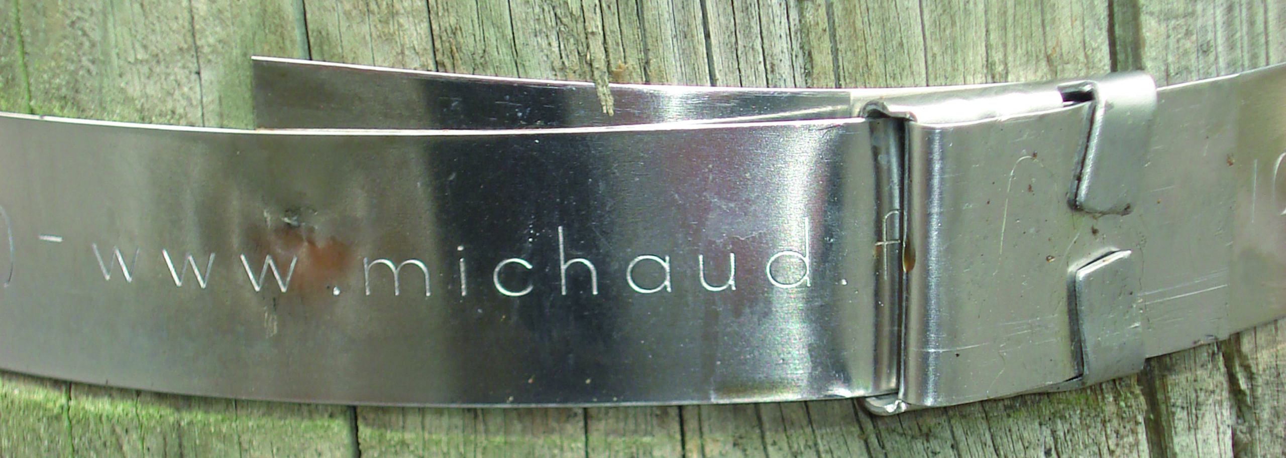 Stainless steel strap Feuillard de la marque MICHAUD installé sur un poteau électrique en bois.